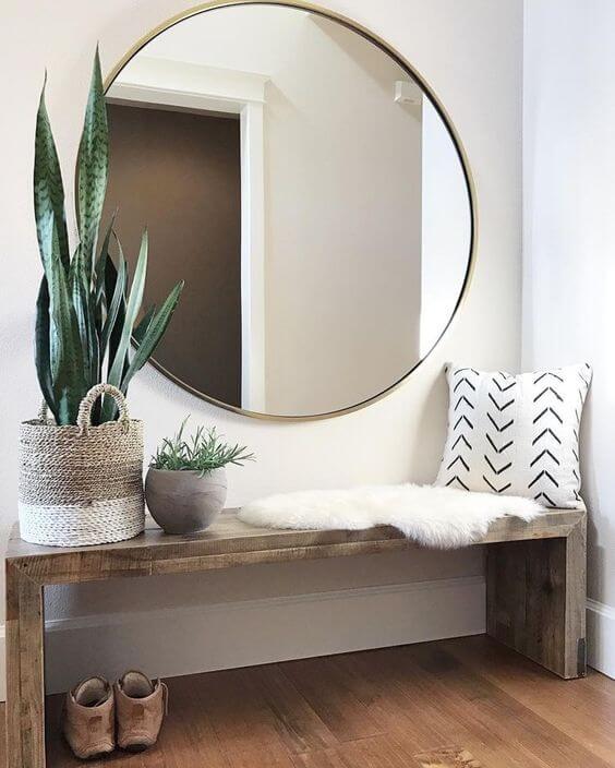 A large round mirror over top a bohemian style bench with a fur rug, plants and a throw pillow