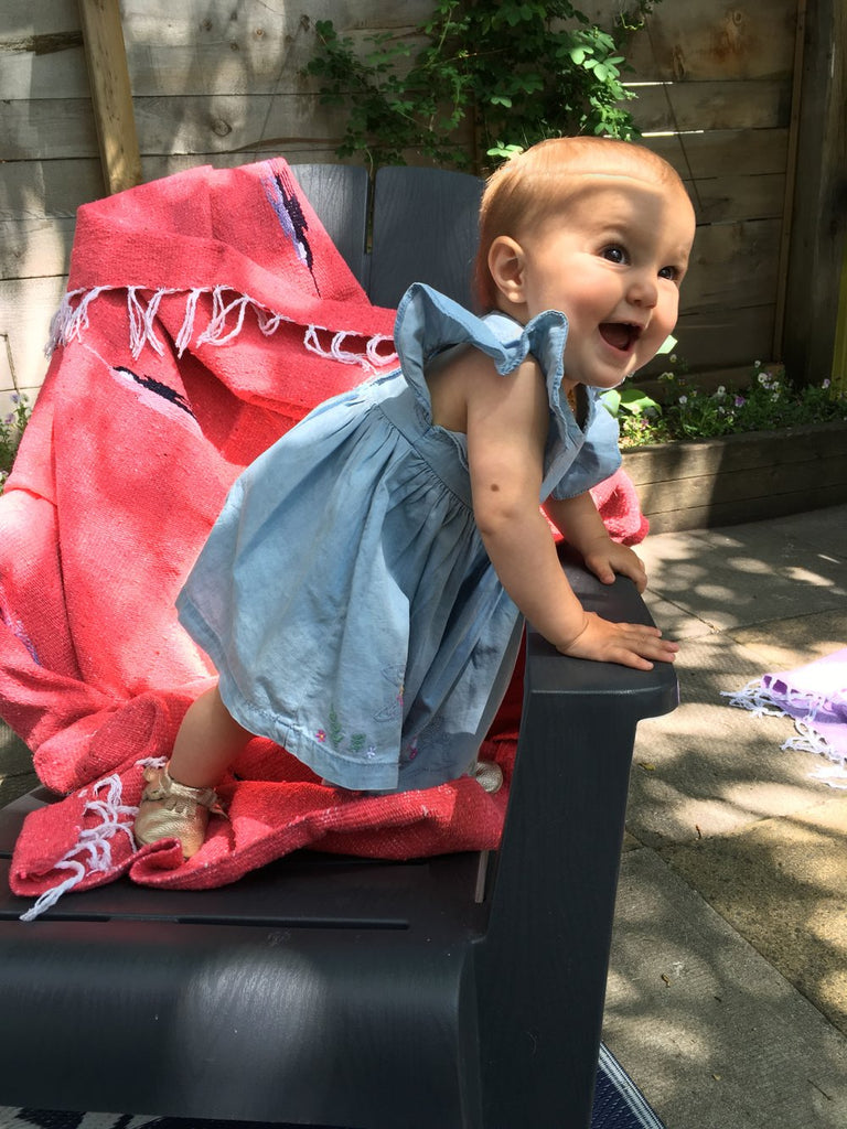 coral coloured mexican blanket on a deck chair with a baby in a blue dress